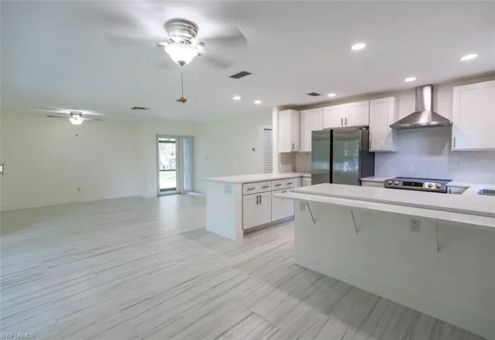 Kitchen featuring wall chimney range hood, kitchen peninsula, white cabinets, and appliances with stainless steel finishes