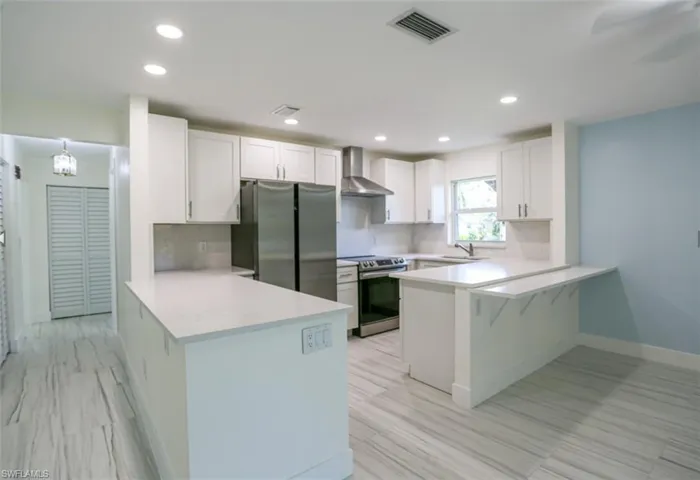 Kitchen featuring appliances with stainless steel finishes, tasteful backsplash, white cabinetry, kitchen peninsula, and wall chimney exhaust hood