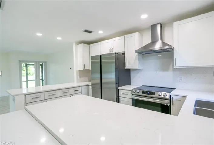 Kitchen with wall chimney exhaust hood, light stone counters, kitchen peninsula, and appliances with stainless steel finishes