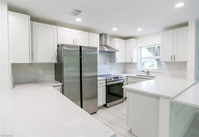 Kitchen featuring decorative backsplash, white cabinets, wall chimney range hood, and appliances with stainless steel finishes