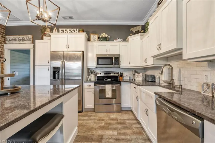 Kitchen featuring white cabinets, appliances with stainless steel finishes, decorative light fixtures, and dark stone counters