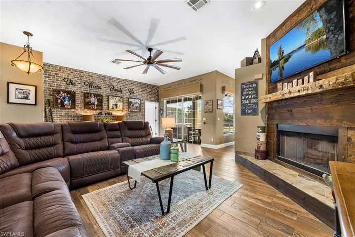 Living room featuring wood-type flooring, ceiling fan, and brick wall