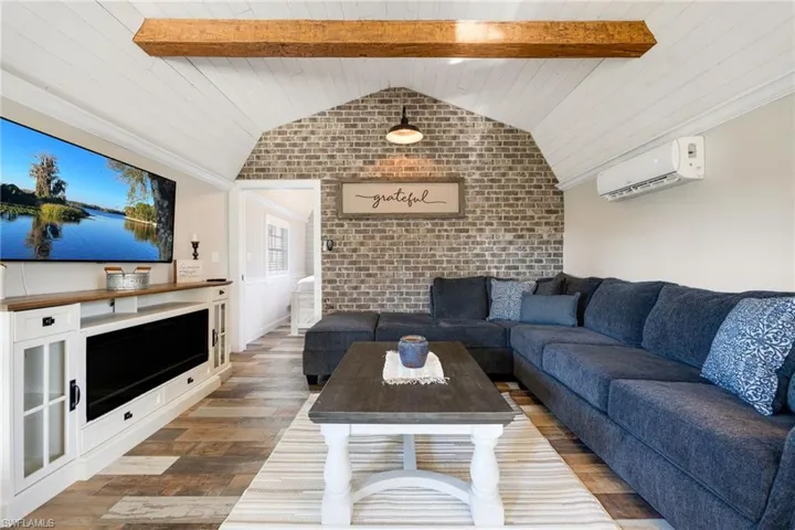 Living room featuring brick wall, a wall mounted air conditioner, wood-type flooring, vaulted ceiling with beams, and wood ceiling