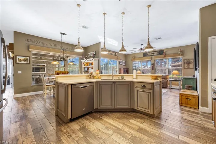 Kitchen with decorative light fixtures, an island with sink, sink, stainless steel dishwasher, and light hardwood / wood-style flooring