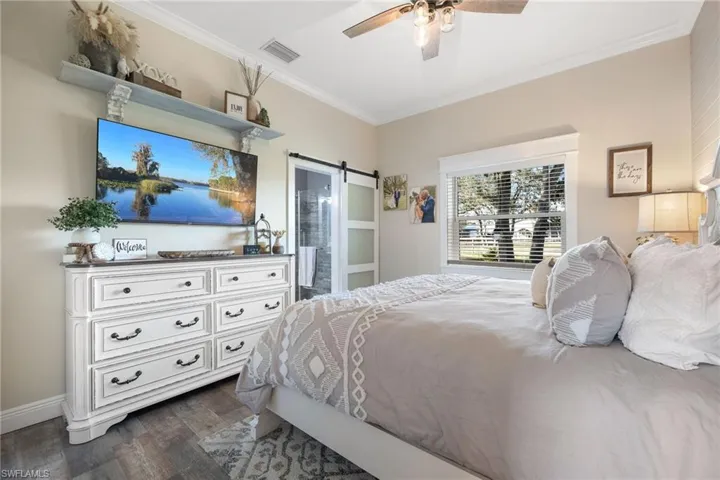 Bedroom featuring dark wood-type flooring, connected bathroom, crown molding, ceiling fan, and a barn door