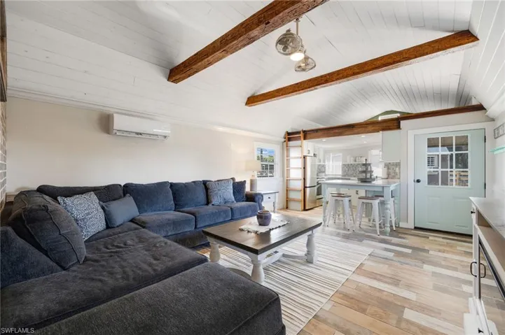 Living room featuring vaulted ceiling with beams, wooden ceiling, light hardwood / wood-style flooring, and an AC wall unit
