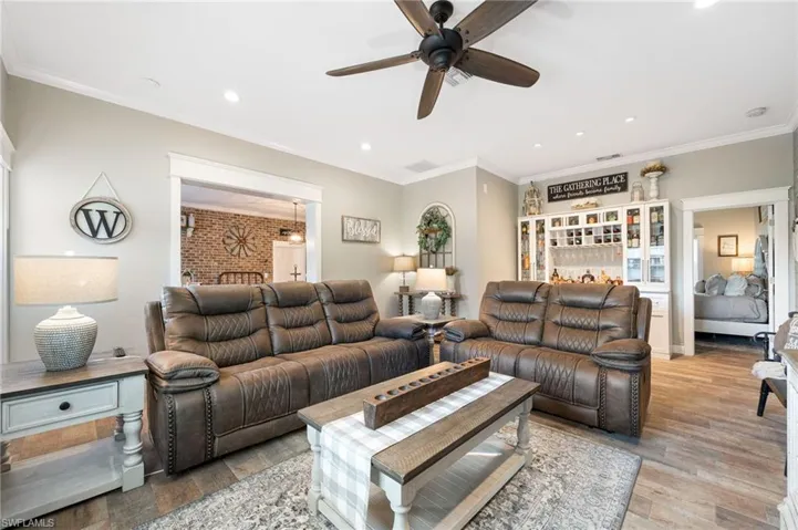 Living room featuring crown molding, wood-type flooring, ceiling fan, and brick wall