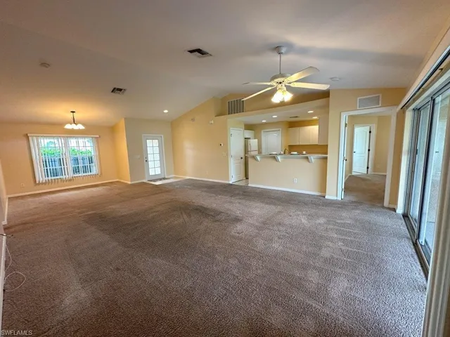 Unfurnished living room with ceiling fan with notable chandelier, lofted ceiling, and light colored carpet