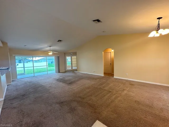 Unfurnished living room with ceiling fan with notable chandelier, vaulted ceiling, and carpet