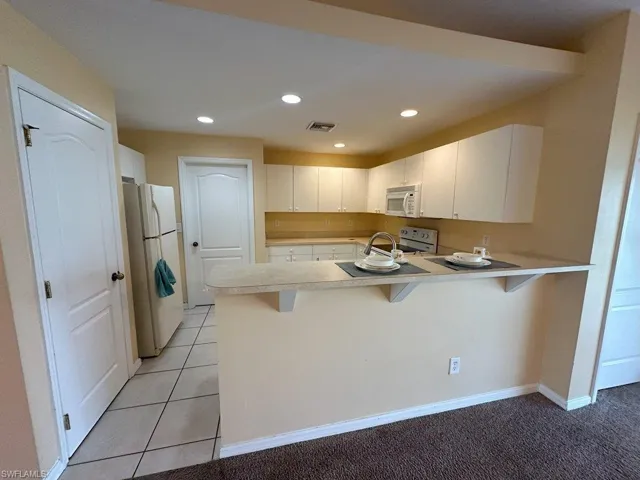 Kitchen featuring white appliances, a kitchen breakfast bar, light carpet, white cabinetry, and kitchen peninsula