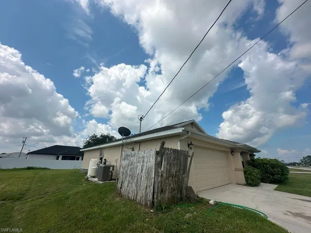 View of side of property featuring a lawn, central AC unit, and a garage
