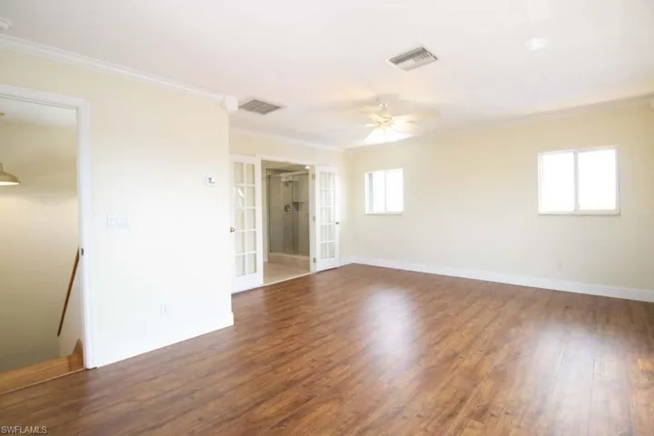 Empty room featuring crown molding, french doors, dark wood-style floors, and ceiling fan