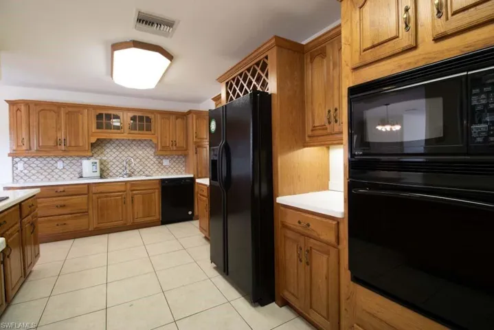 Kitchen with brown cabinets, glass insert cabinets, light countertops, and black appliances