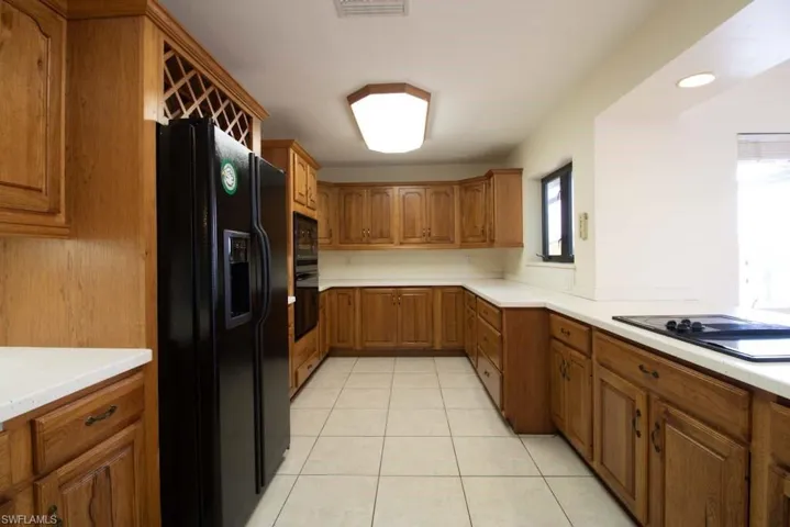 Kitchen featuring light tile patterned floors, brown cabinets, a breakfast bar, light countertops, and recessed lighting