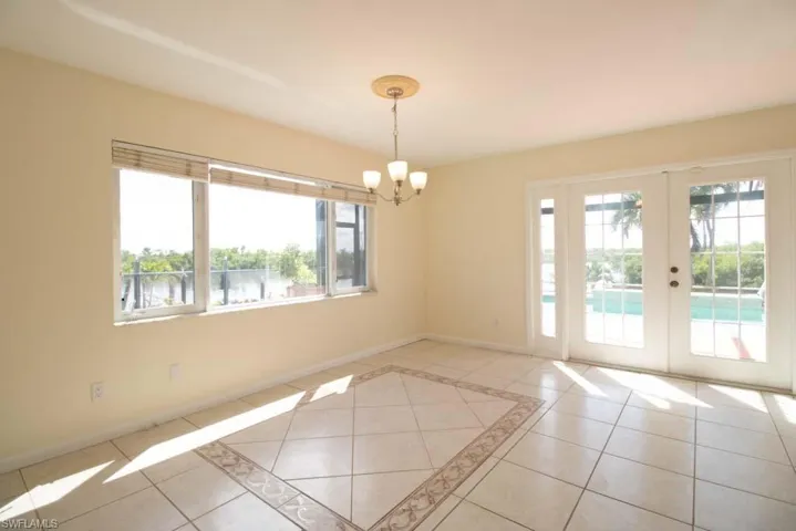 Empty room with light tile patterned flooring, inlaid floor details, french doors, a water view, and a chandelier