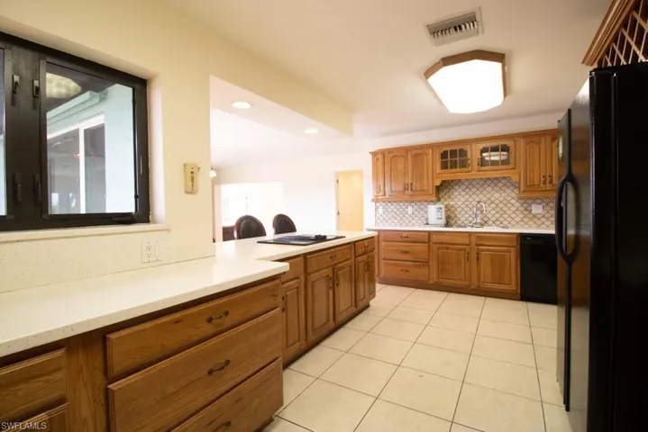 Kitchen featuring tasteful backsplash, glass insert cabinets, brown cabinetry, black appliances, and light tile patterned flooring