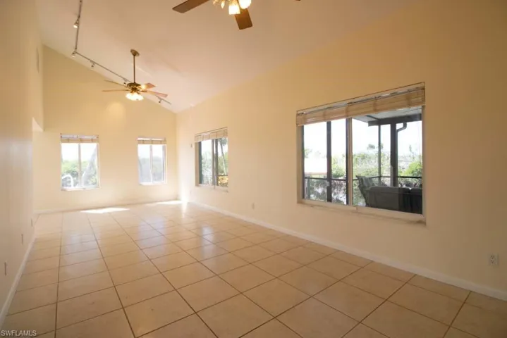 Empty room featuring light tile patterned floors, rail lighting, high vaulted ceiling, a chandelier, and a ceiling fan