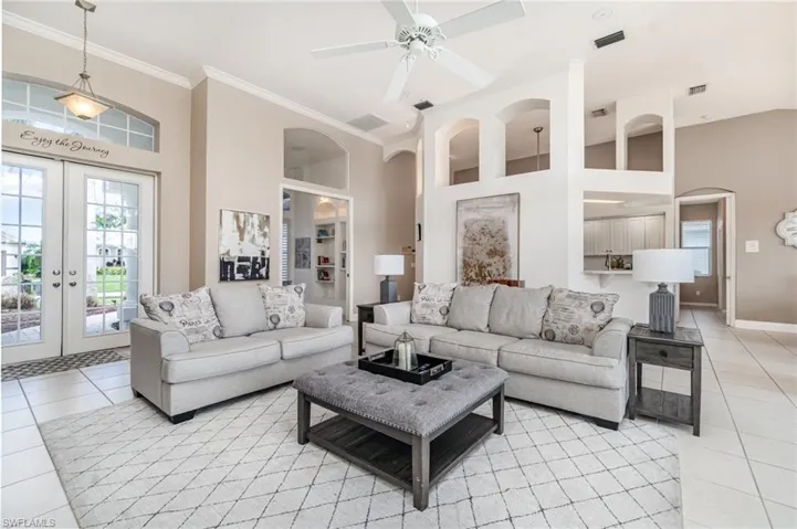 Living room with light tile patterned floors, french doors, a high ceiling, a ceiling fan, and crown molding