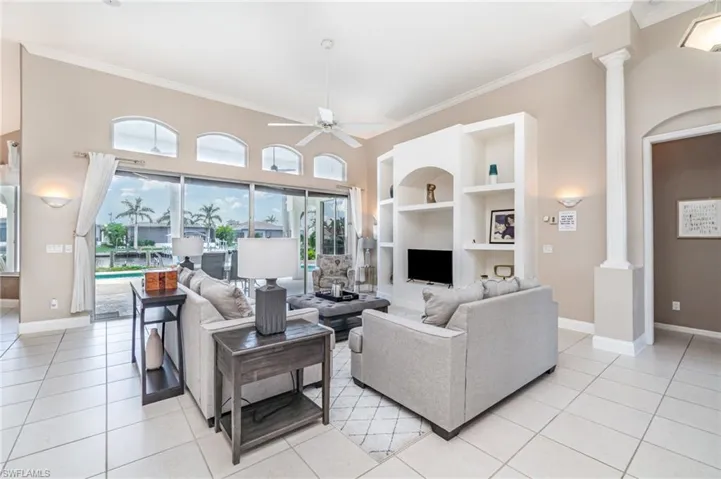 Living area with ornamental molding, light tile patterned flooring, ceiling fan, and built in features