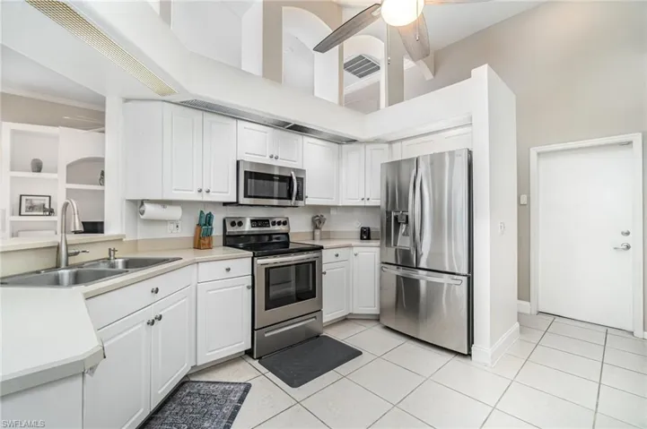 Kitchen with stainless steel appliances, white cabinets, light countertops, and a high ceiling