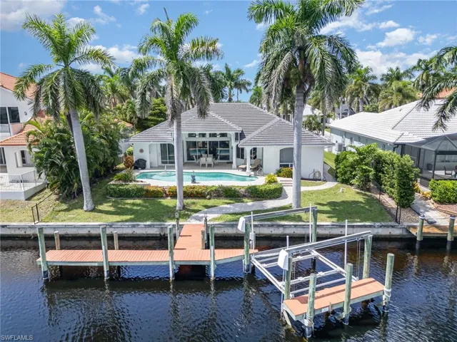 Back of house featuring boat lift, a patio area, a water view, and an outdoor pool