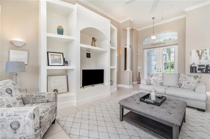 Tiled living area with built in features, crown molding, french doors, decorative columns, and ceiling fan