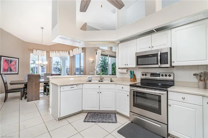 Kitchen with appliances with stainless steel finishes, a peninsula, hanging light fixtures, white cabinets, and light countertops