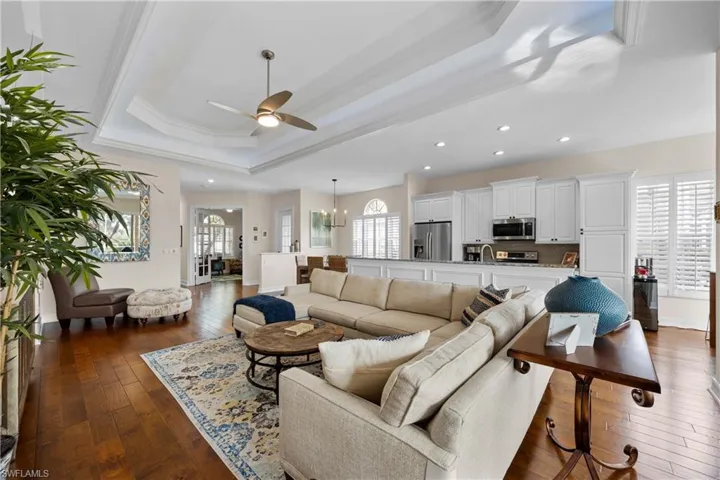 Living room with a tray ceiling, dark hardwood / wood-style flooring, ceiling fan with notable chandelier, and ornamental molding