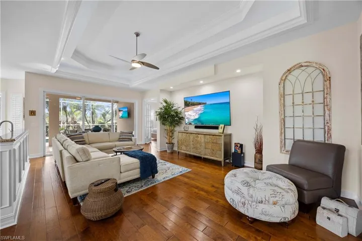 Living room featuring ceiling fan, crown molding, dark wood-type flooring, and a tray ceiling
