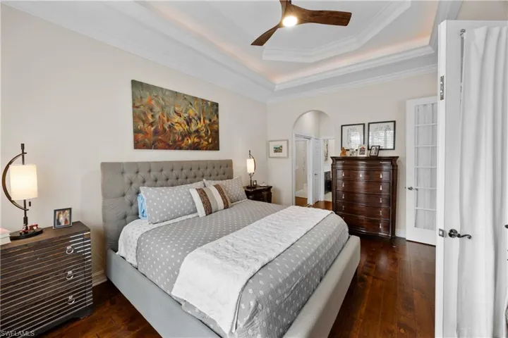 Bedroom featuring french doors, a raised ceiling, ceiling fan, dark wood-type flooring, and crown molding