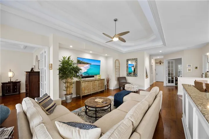Living room with a tray ceiling, crown molding, ceiling fan, and dark hardwood / wood-style floors