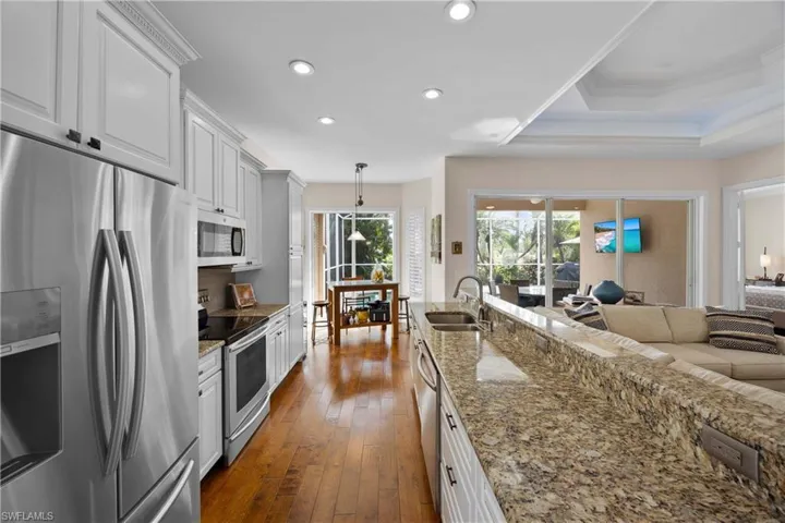 Kitchen featuring white cabinets, dark hardwood / wood-style floors, decorative light fixtures, light stone counters, and stainless steel appliances