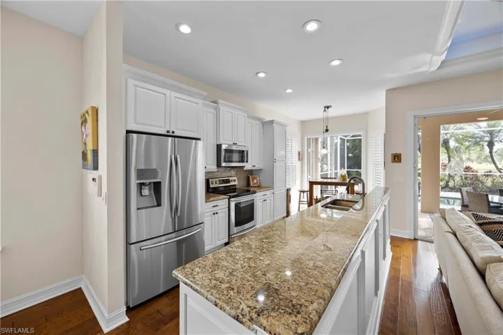Kitchen with appliances with stainless steel finishes, pendant lighting, a center island with sink, white cabinets, and dark hardwood / wood-style floors