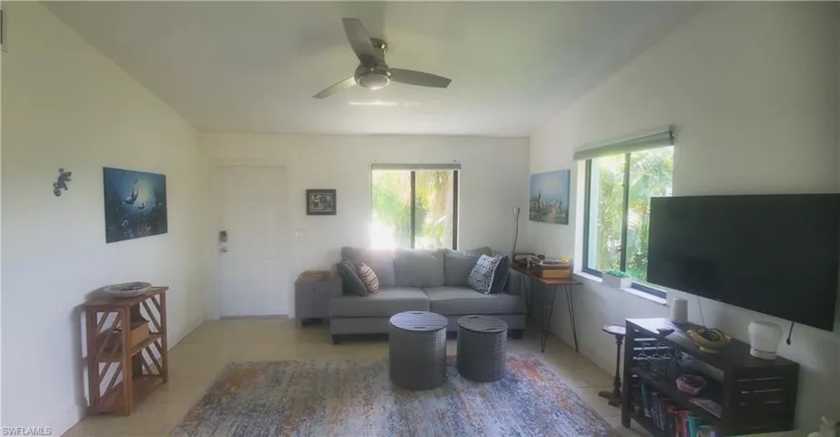 Living room featuring ceiling fan, light tile patterned flooring, and lofted ceiling