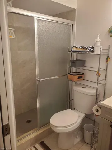 Bathroom featuring a shower with shower door, vanity, tile patterned floors, and toilet