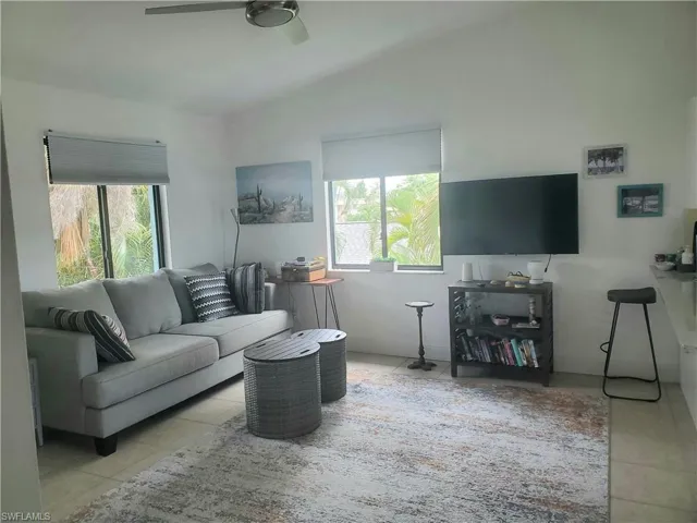 Living room featuring ceiling fan, light tile patterned flooring, and lofted ceiling