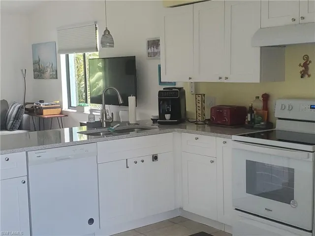 Kitchen with white cabinetry, Whirlpool dishwasher and stove, custom range hood, light tile floor and sink