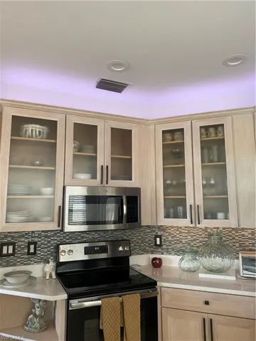 Kitchen with range, light brown cabinets, backsplash, and glass insert cabinets