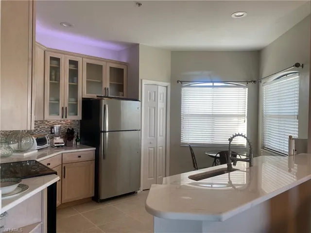 Kitchen with glass insert cabinets, black electric range, freestanding refrigerator, light stone counters, and light tile patterned flooring