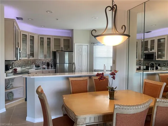 Kitchen with glass insert cabinets, decorative backsplash, appliances with stainless steel finishes, a breakfast bar area, and a peninsula