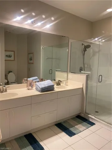 Full bath with double vanity, light tile patterned floors, and a stall shower