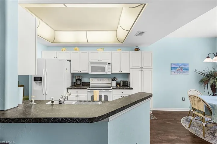 Kitchen featuring dark countertops, white cabinetry, white appliances, a peninsula, and dark wood finished floors