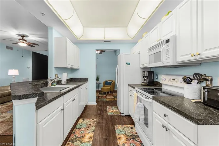 Kitchen featuring dark countertops, ceiling fan, white appliances, white cabinetry, and dark wood finished floors