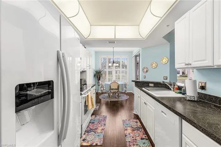 Kitchen with white appliances, white cabinets, dark wood-type flooring, and dark countertops