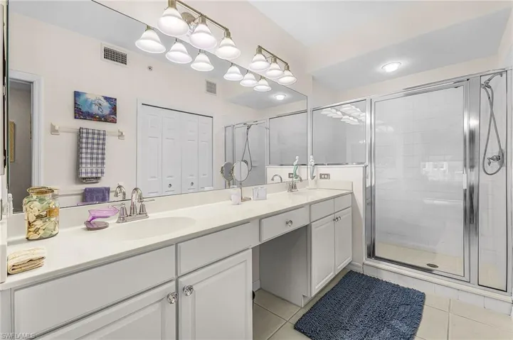 Full bathroom with a closet, double vanity, a shower stall, and light tile patterned floors