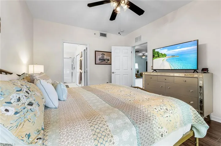 Bedroom with dark wood-type flooring, a ceiling fan, and connected bathroom