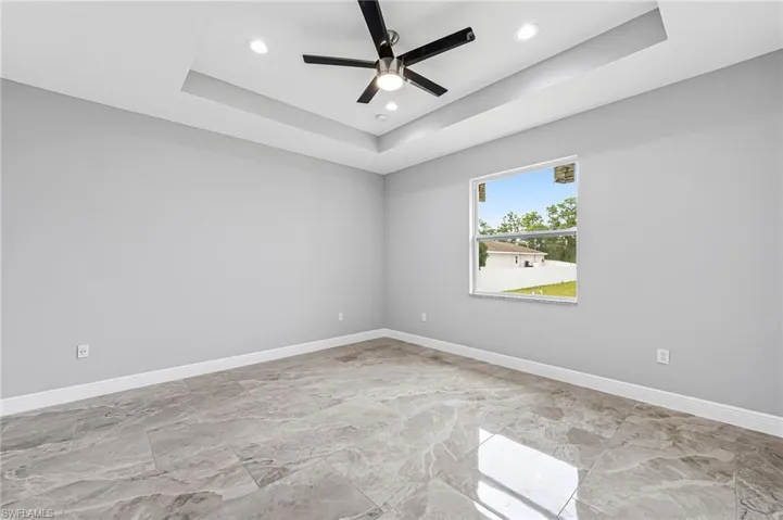 Empty room featuring ceiling fan, light tile floors, and a raised ceiling