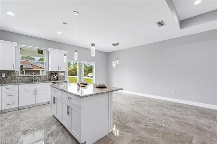 Kitchen featuring decorative light fixtures, backsplash, light tile floors, a center island, and white cabinets