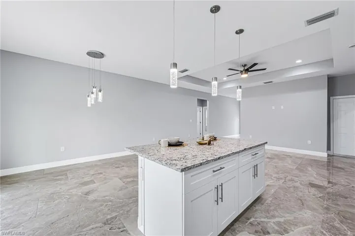 Kitchen featuring ceiling fan, decorative light fixtures, light stone counters, a center island, and white cabinetry
