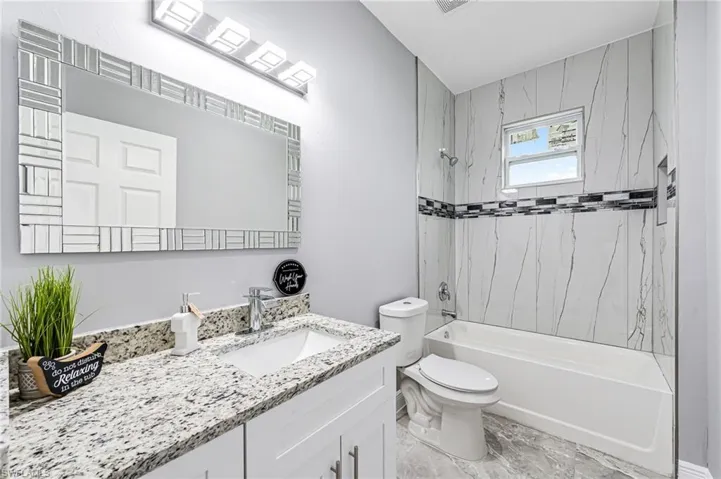 Full bathroom with tile flooring, tiled shower / bath, oversized vanity, and toilet